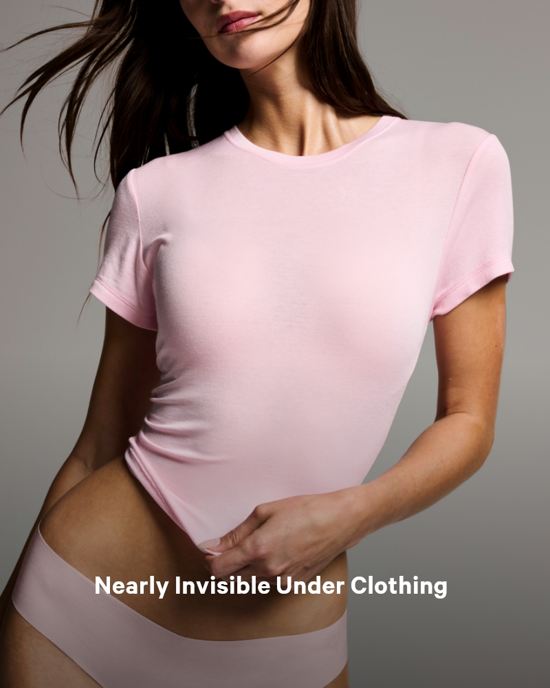 Woman posing in a baby pink t-shirt and panties on a gray background.