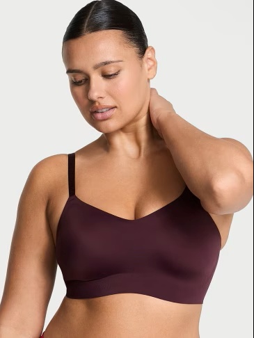 Woman posing in a Victoria's Secret dark red bralette on a light grey background.