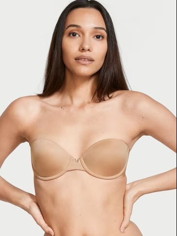 Woman posing in a Victoria's Secret beige strapless bra on a light grey background.