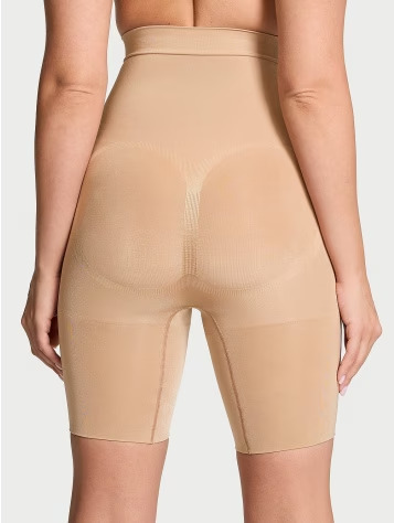 Back view of a woman wearing Victoria's Secret beige lower body shapewear on a light grey background